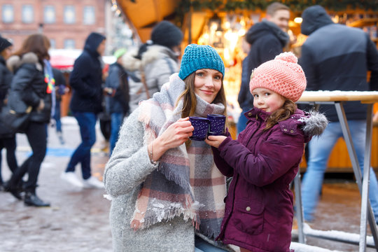 Little cute daughter and mother with cup of steaming hot chocolate or children punch. Happy child girl and beautiful woman on Christmas market in Germany. Traditional leisure for families on xmas.