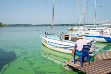 Obraz premium Fisherman catches fish near yachts. Senor fishermen on the quay of the yacht club