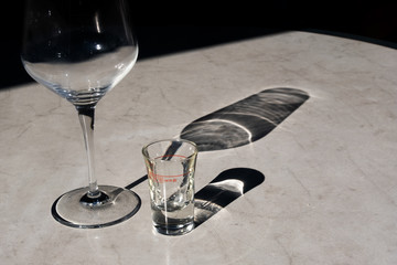  Kunststoff Marmor Imitation Tisch in Restaurant Terrasse nach dem Essen mit leerem Wein glass und leerem Aperetiv Grappa Ouzo Schnaps Glass mit schönem Schatten horizontal.