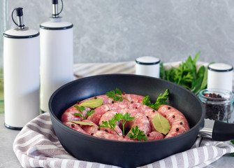 Meat sausages in frying pan, with bay leaves and fresh herbs in the kitchen