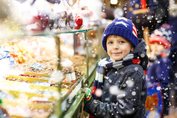 Little cute kid boy near sweet stand with gingerbread and nuts. Happy child on Christmas market in...