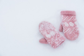 Soft, warm, pink knitted mittens on the white snow