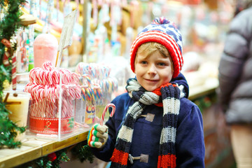 Little cute kid boy buying sweets from a cancy stand on Christmas market. Happy child on traditional family market in Germany. Preschooler in colorful winter clothes..
