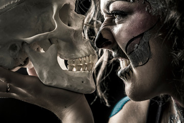 Portrait of the woman with halloween makeup close up. Talking with skull, which is in front of her. Isolated image on black background with the smoke and beautiful studio light.