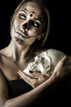 Portrait of the woman with halloween makeup close up. Playiong with skull. Isolated image on black background with beautiful studio light.