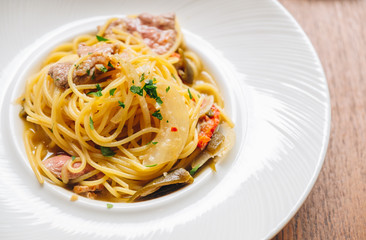 Spaghetti spicy with bacon, dry chili, green olive in white dish top view on wooden background. 