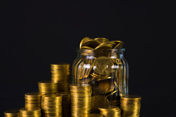 Coins stacks and gold coin money in the glass jar on dark background, for saving for the future banking finance concept.