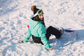 Fototapeta na wymiar Leisure, sport concept - woman snowboarder sitting on snow