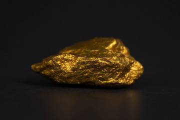 Closeup of gold nugget or gold ore on black background, precious stone or lump of golden stone, financial and business concept.