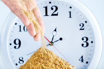 Sand flows from the hand of man on clock background. Concept of time.