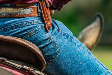 Lovely crafted belt and knife carrier and brown leather saddle, american cowboy warming up before rodeo performance on new ranch. Sunny event, United States national culture.