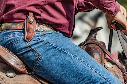 Lovely crafted belt and knife carrier and brown leather saddle, american cowboy warming up before rodeo performance on new ranch. Sunny event, United States national culture.