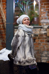 young woman in  fur coat, hat and snood on background  brick wall