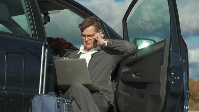 Businessman with a laptop suitcase working relaxing on the beach near his car.
