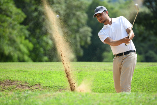 Young Asian man golfer hitting a bunker shot