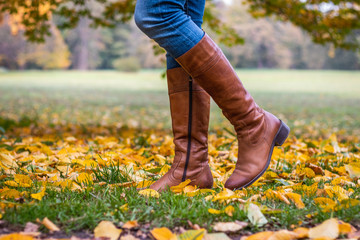 Woman wearing brown leather boot and walking in fallen leaves. Fashion model in autumn park 