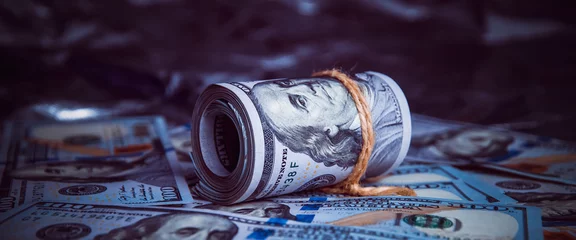 In the dark on broken money is a roll of dollars lit by a ray of light. © andreyphoto63