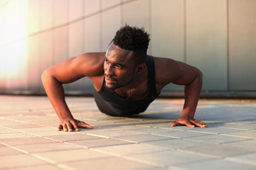 Fototapeta premium African man in sports clothing keeping plank position while exercising outdoors.