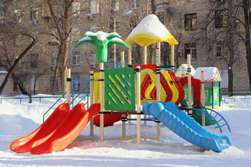 New slides on the kids Playground place close up on the background of a multi-storey house in snowy winter day - game rides for children on the outdoor