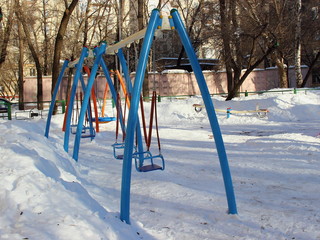 Blue swings on the Playground in snow winter - attractions for children outdoor activity