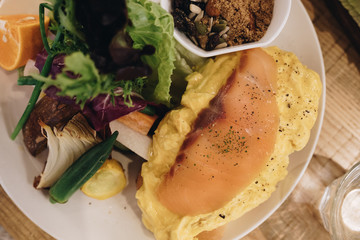 Eggs Benedict on english muffin with smoked salmon, lettuce salad mix and hollandaise sauce on white plate