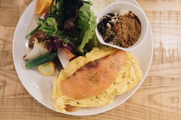 Eggs Benedict on english muffin with smoked salmon, lettuce salad mix and hollandaise sauce on white plate