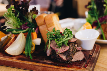 Sliced grilled beef barbecue beef steak and salad with tomatoes onion and arugula on cutting board close-up
