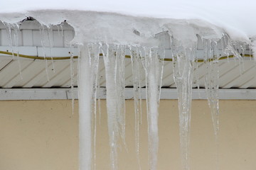 Dangerous icicles on the roof of a stone house in the city - municipal service, drops, thaw, spring in the urban area