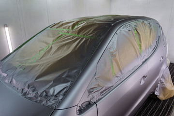 Full painting of a silver car in the back of a hatchback, some parts of which are protected by paper from splashes of paint droplets in a car body repair shop with a special box and equipment