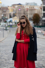 Fototapeta premium Lovely brunette model with long hair wearing red dress and blue coat, posing in the evening city