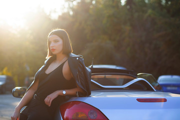 Luxurious brunette lady with red lips, posing in a convertible car with a sun light. Space for text