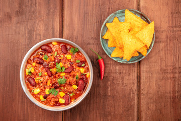 Chili con carne, traditional Mexican dish, shot from the top on a wooden table with nacho chips, a chili pepper and a place for text
