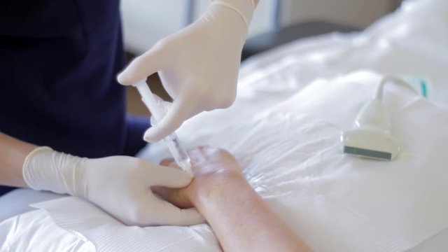 The latex gloved hands of a doctor inject a prolotherapy solution into the wrist of a patient with chronic pain to prompt her body to start the healing process.  