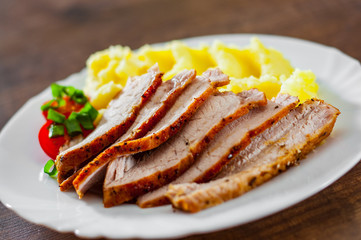 meat slices with mashed potatoes in white plate on wooden table background