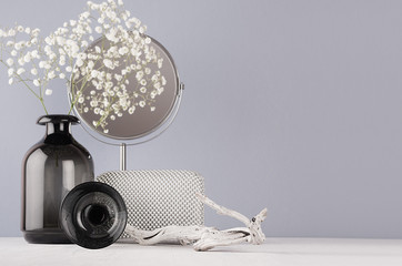 Fashion modern monochrome style in bathroom interior - cosmetic products and accessories, black glass vase with flowers, circle silver mirror, old snag on white wood board and grey wall.