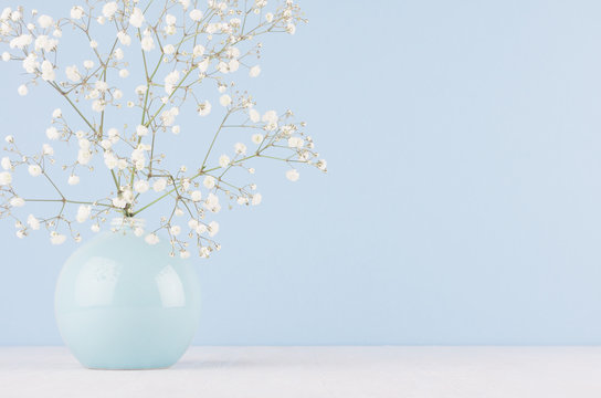 Fototapeta Spring branch with small white flowers in blue sphere vase in soft light blue modern interior, on a white table.