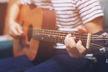 Obraz premium Stylish hipster guy Acoustic Guitar Playing by hand. Artist young male musician Plaid shirt Playing Acoustic Guitar in sofa living room parlor.