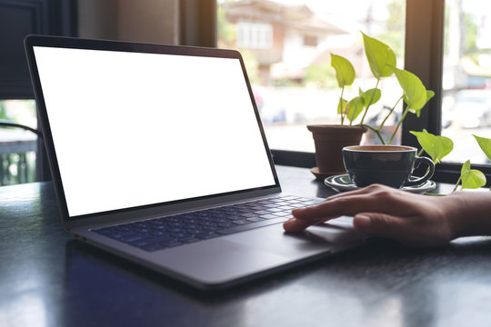 Mockup image of a woman's hands using and touching laptop touchpad with blank white desktop screen with coffee cup on wooden table in cafe