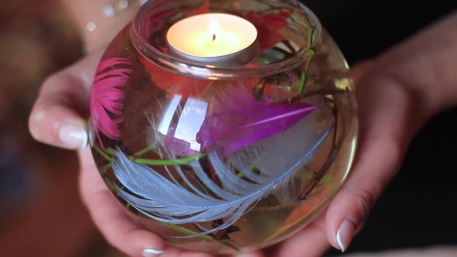 women's hands hold a glass flask with burning candles and decor inside her