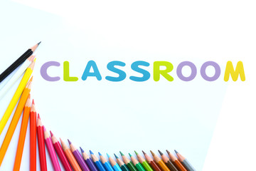 Colored pencils wave with alphabet sponge rubber of text "CLASSROOM" over white background.
