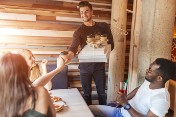 Caucasian sportive man with athletic body handing out food orders to his multiethnic friends at...