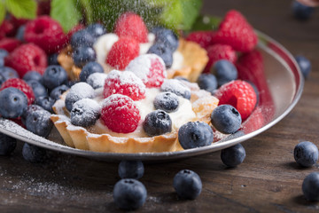  Dessert tarts with raspberries and blueberries on a wooden table.