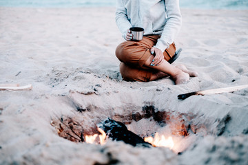 Woman resting near the campfire on beach.