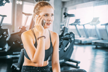 Fototapeta na wymiar Active girl using smartphone in fitness gym.Young smiling woman at the gym relaxing and listening to music using a mobile phone