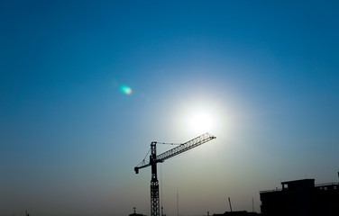 Industrial construction crane and building silhouettes over sun at sun and blue sky