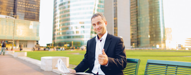 Happy male manager reading newspaper and smiling outside in  . Concept of businessman and mass...