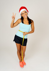 Fit young woman in Santa hat measuring her waist feeling happy and showing victory and ok gestures