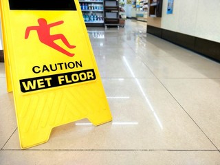 Warning sign beware slippery floor on tiles floor of aisle inside supermarket, sign and symbol...