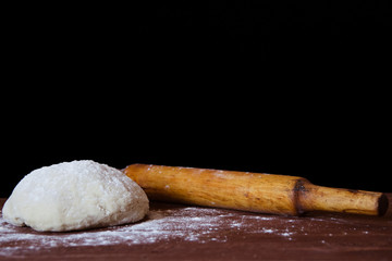 Fototapeta na wymiar a lump of dough and a rolling pin lie on a wooden table on a black background