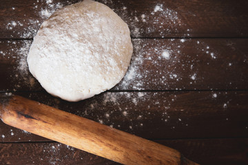 a lump of dough and a rolling pin lie on a wooden table